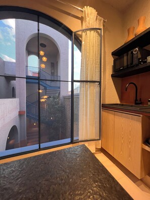 Eine moderne Küche mit einem großen Fenster, einer schwarzen Arbeitsplatte, Holzschränken und einer Mikrowelle auf einem Regal.