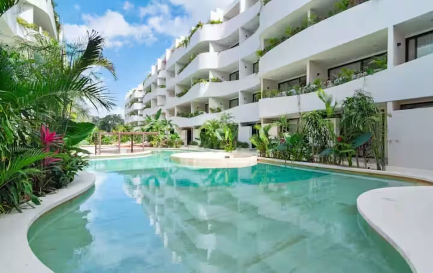 Um hotel moderno com piscina central, rodeado por vegetação exuberante e varandas brancas.