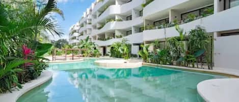 A modern hotel with a central swimming pool, surrounded by lush greenery and white balconies.