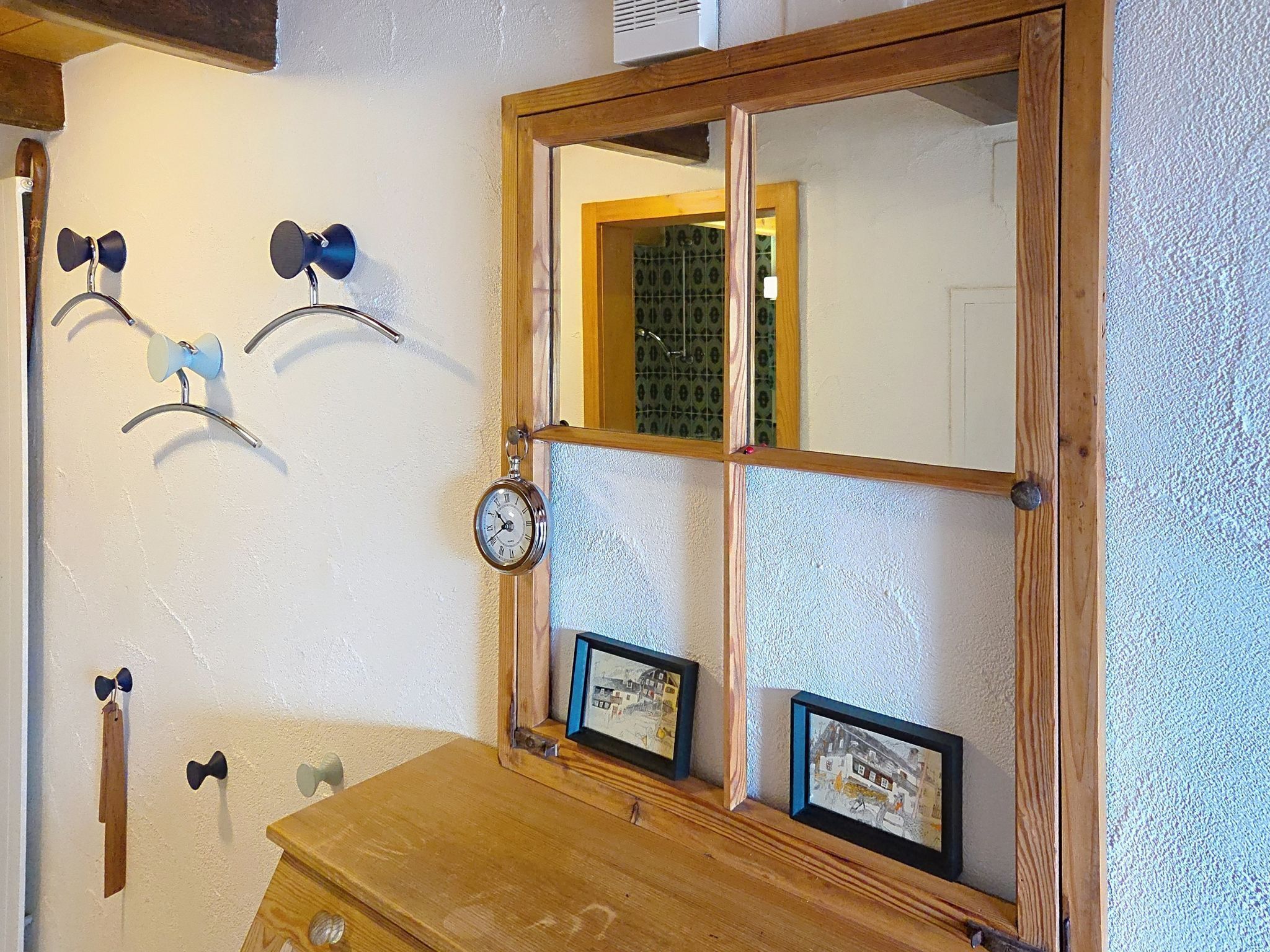 A wooden dresser with a mirror, a clock, and two framed pictures on the wall.