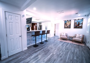 A modern kitchen with bar stools, a dining area with two sofas, and a living room with a rug.