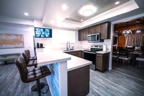 A modern kitchen with a central island, dark wooden cabinets, stainless steel appliances, and a dining area with a chandelier.
