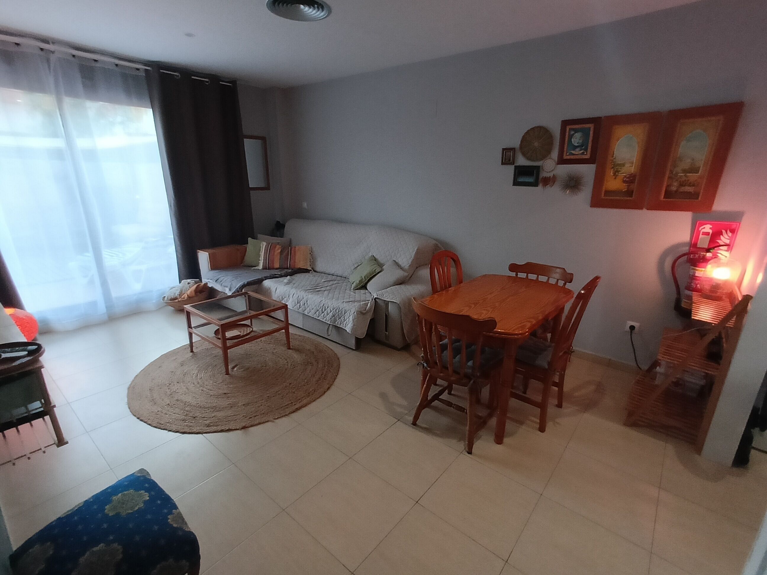 Una sala de estar con un sofá, una mesa de comedor con sillas, una mesa de centro, una alfombra y un calentador fijado a la pared.