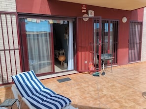 Ein Zimmer mit einem gestreiften Stuhl, einem kleinen Tisch, einem Fliesenboden und einer Glasschiebetür, die auf einen Balkon führt.
