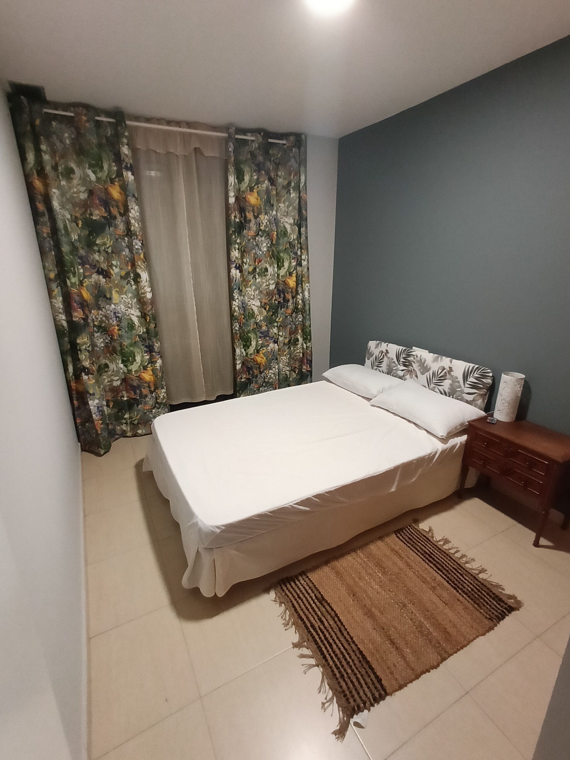 Un dormitorio con cama, cortinas, una mesita de noche y una alfombra.