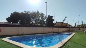 En rektangulär swimmingpool med en vit kant, omgiven av konstgräs, och en klar himmel ovanför.