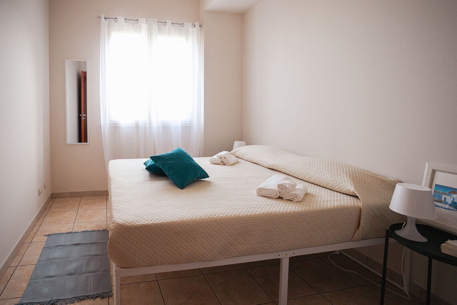 Un lit simple avec un oreiller turquoise, des serviettes blanches et une petite table sur laquelle se trouve une lampe.