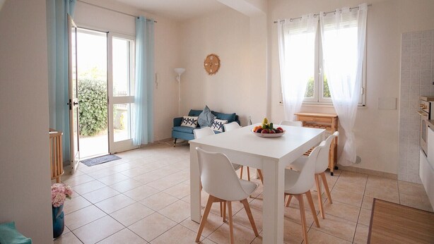 A dining area with a white table and chairs, a blue sofa, and a kitchen in the background. - Mediterranea - Seaside Sicily Home with Veranda (Marina di Modica (Modica))
