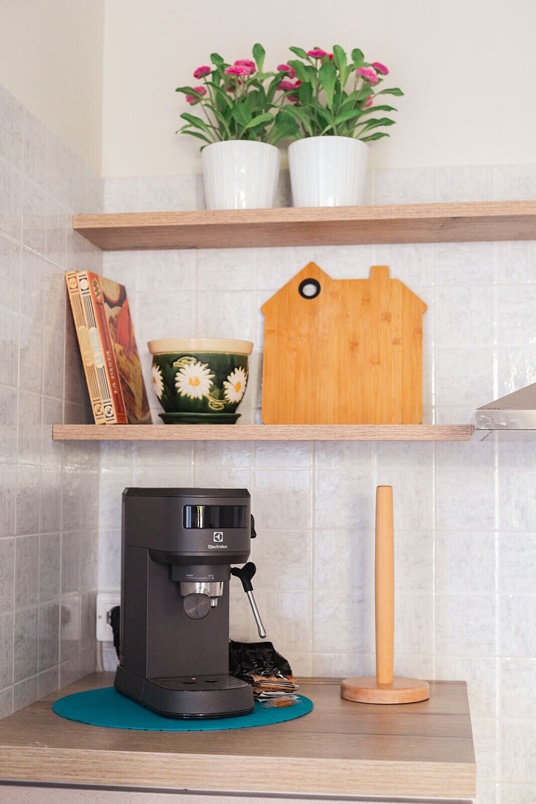 A kitchen with a coffee maker, a wooden cutting board, a potted plant, and a decorative house-shaped item on a shelf.