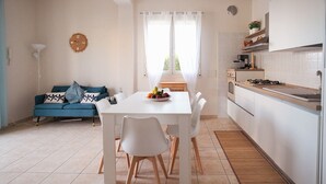 A modern kitchen with white cabinets, a dining table with chairs, and a blue sofa with decorative pillows. - Mediterranea - Seaside Sicily Home with Veranda (Marina di Modica (Modica))