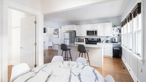 Eine moderne Küche mit weißen Schränken, einem Esstisch aus Marmor und Blick zum Wohnbereich.