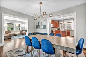 Ein moderner Essbereich mit einem Holztisch und blauen Stühlen, eine Küche mit Holzausbau und ein Wohnzimmer mit einer Couch und einem Couchtisch.