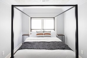 Une chambre à coucher moderne avec un lit à baldaquin, deux tables de chevet et une grande fenêtre laissant entrer la lumière naturelle.