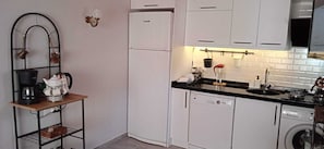 Cozinha compacta com armários brancos, lava-louças, cafeteira e chaleira em uma prateleira.
