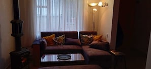 A cozy living room with a sofa, a table, a lamp, and a wood-burning stove.