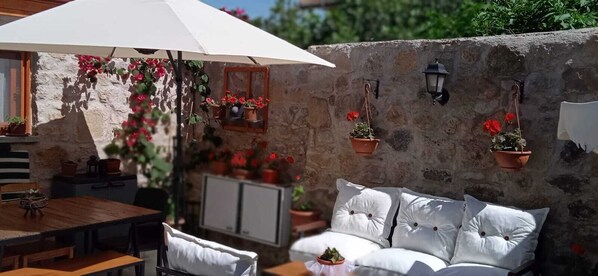 A stone wall with hanging flower pots, a white umbrella, and a white sofa with cushions.