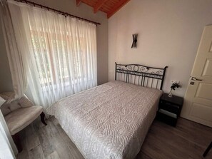 A bedroom with a bed, a chair, a bedside table, and a door.