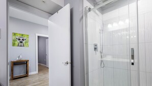 Um banheiro moderno com box de vidro, mesa lateral de madeira com um objeto decorativo e um quadro na parede.