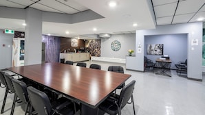 Uma sala de conferências moderna com uma mesa comprida, cadeiras, um espaço de cozinha e um relógio na parede.