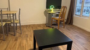 A room with a wooden floor, a desk with a computer, a chair, and a table.