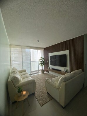 A living room with a sofa, a TV, a plant, and a small table with a candle. - Ocean View - family Apartment- 15min Airport & Miraflores in San Miguel Lima (San Miguel)
