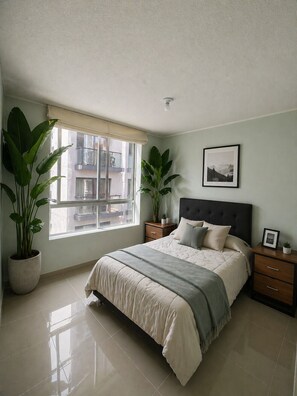 A bedroom with a bed, bedside tables, a window, and potted plants. - Ocean View - family Apartment- 15min Airport & Miraflores in San Miguel Lima (San Miguel)