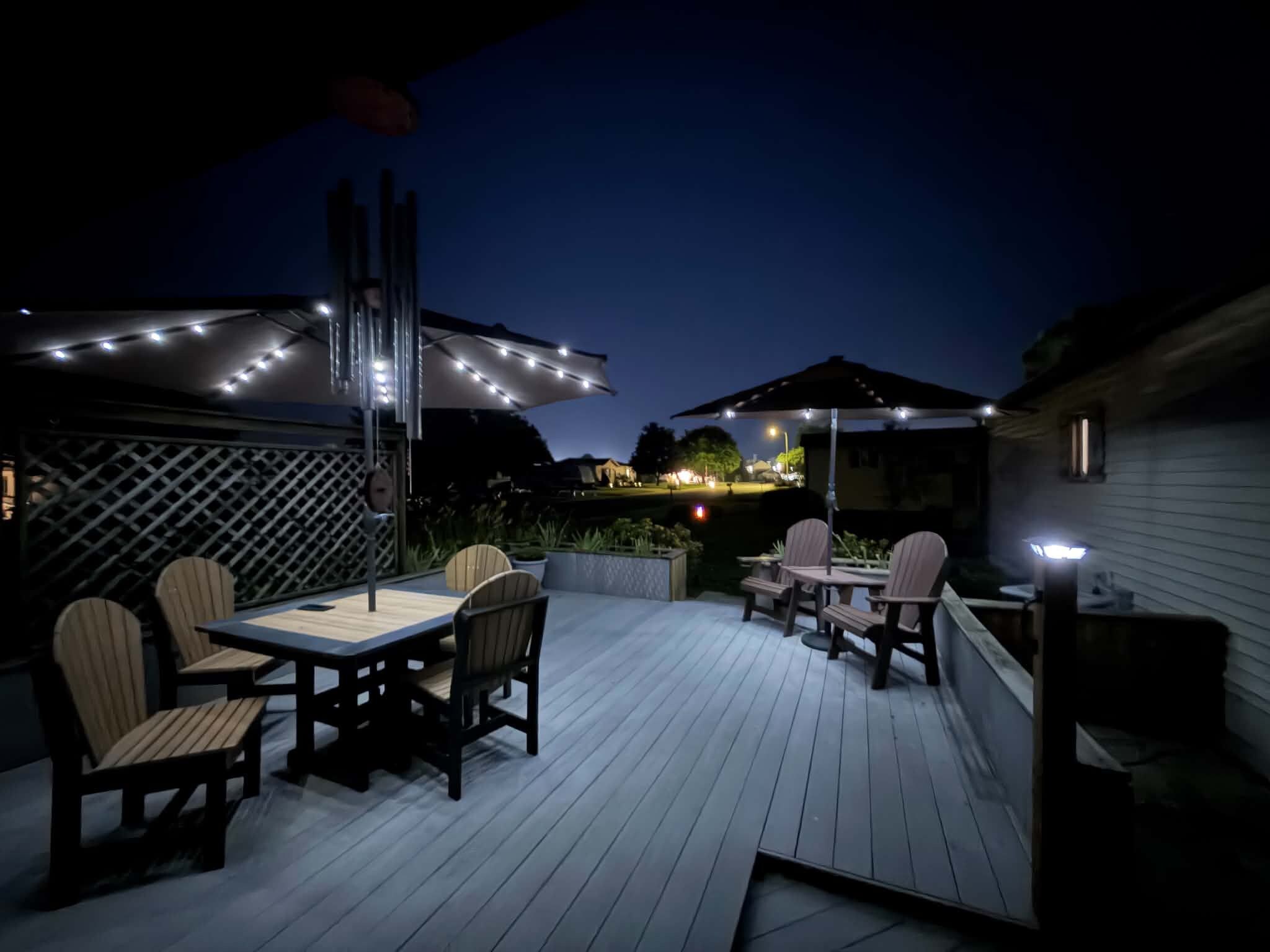 An outdoor deck with a table and chairs, string lights, and umbrellas.
