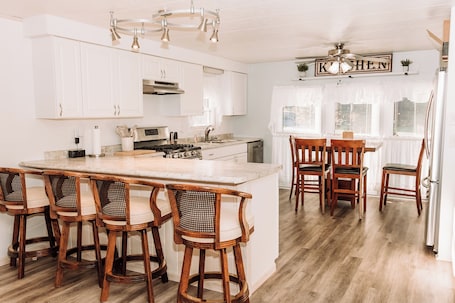 A kitchen with white cabinets, a central island with bar stools, a dining table with chairs, and a ceiling fan.. Cozy 2 Bedroom Home in Prairie du Chien - Make a Memory