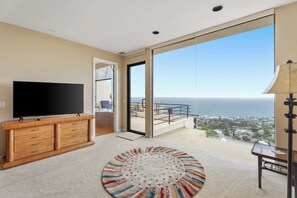 Ein modernes Wohnzimmer mit Flachbildfernseher, einer Holzkommode, einem bunten Teppich und einem Balkon mit Meerblick.