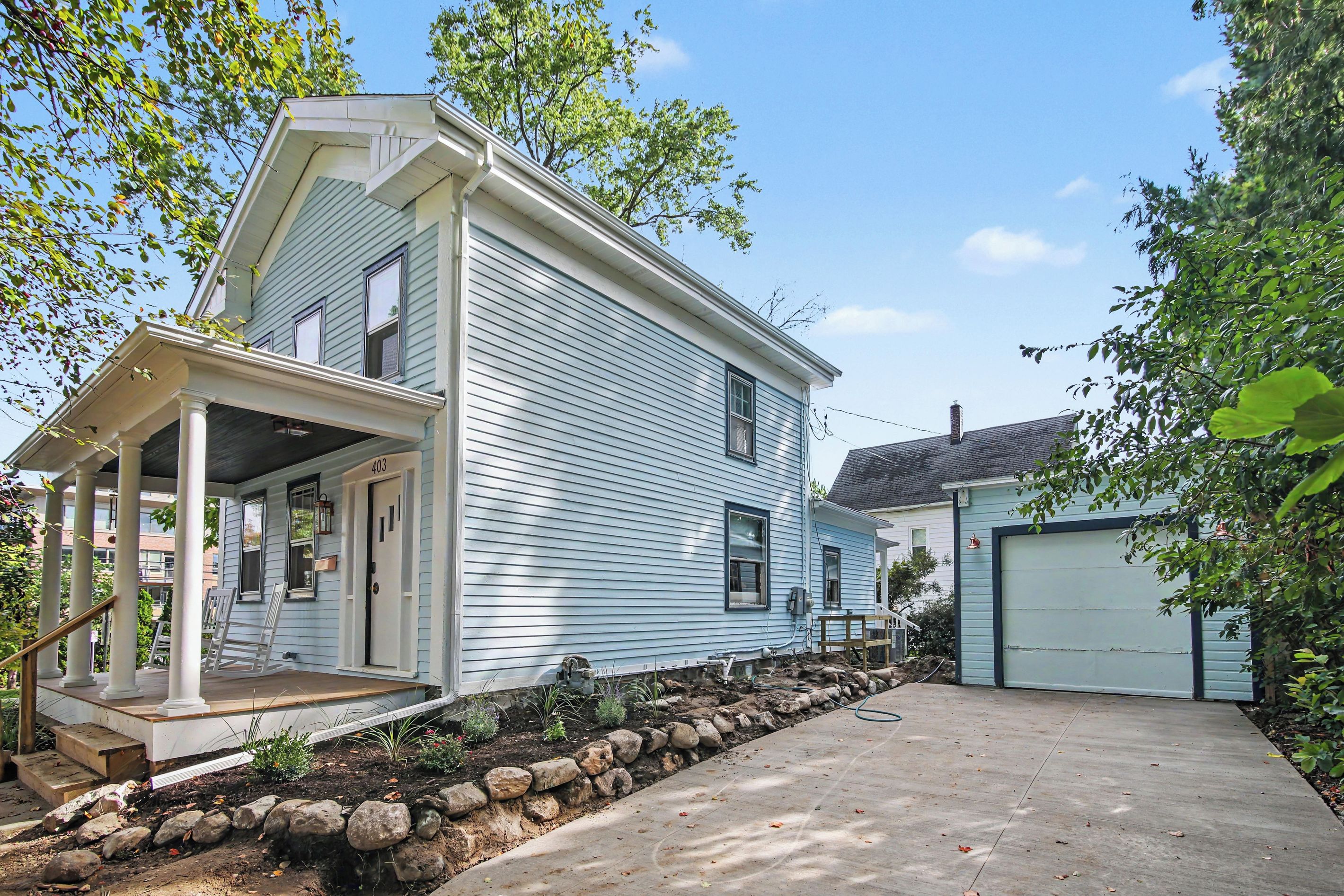 A two-story house with a porch, a garage, and a stone retaining wall.