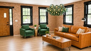 A room with a brick wall, large windows, a green armchair, a brown leather sofa, and a wooden coffee table. - #1 Location I Fully Rebuilt 2026 I .9 Miles to Stadium/2.5 Blocks Downtown (Ann Arbor)