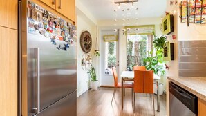 Et moderne køkken med et rustfrit stål køleskab, træskabe, et spisebord med orange stole og udsigt til haven gennem vinduet.