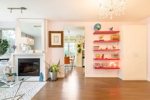 A modern living room with a fireplace, a dining area, and a red bookshelf.