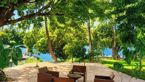 Un espace extérieur aménagé avec des chaises et des tables, entouré d’arbres et offrant une vue sur l’eau.