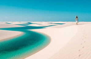 A person walking on a sandy beach with clear blue water.