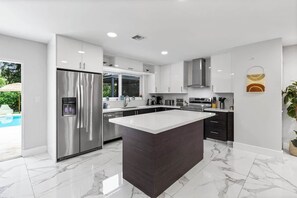 A modern kitchen with a central island, stainless steel appliances, and a view of the outdoors. - Villa Solstice | Heated Pool • Covered Terrace (Miami)