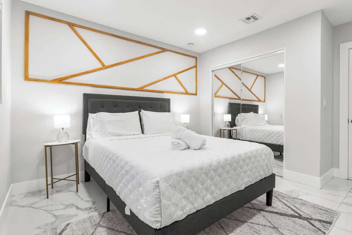 Quarto moderno com uma cama grande, mesas de cabeceira e um espelho.