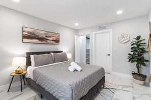 A modern bedroom with a bed, bedside lamp, artwork, closet, and a potted plant. - Villa Solstice | Heated Pool • Covered Terrace (Miami)