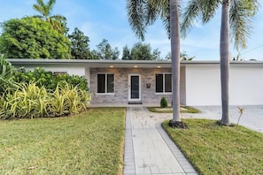 A modern house with a paved driveway, a front door, and a small garden with palm trees and plants. - Villa Solstice | Heated Pool • Covered Terrace (Miami)