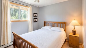 Een slaapkamer met een bed, een nachtkastje, een lamp, een plafondventilator en een raam met gordijnen.