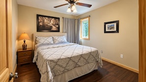 A bedroom with a bed, a nightstand, a lamp, a ceiling fan, and two framed pictures on the walls.
