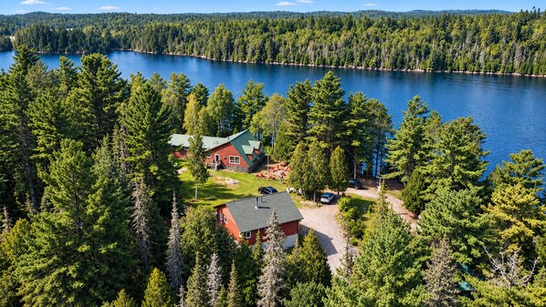 Punaisilla seinillä ja vihreällä katolla varustettu talo, jonka ympärillä on tiheä metsä ja järvi.