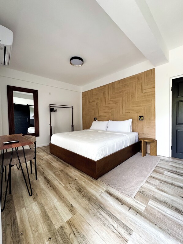 Ein modernes Schlafzimmer mit einem großen Bett, einem Holz-Kopfteil, einem Nachttisch, einem Schreibtisch mit Stuhl und einem Spiegel.