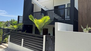 A modern two-story house with a staircase, a wooden fence, and potted plants. - Luxury 2 Bedroom Condo, 5 mins from UVF (Vieux Fort)