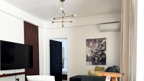 A modern living room with a flat-screen TV, a round orange chair, a wooden coffee table, a green sofa, and a wooden side table. - Luxury 2 Bedroom Condo, 5 mins from UVF (Vieux Fort)