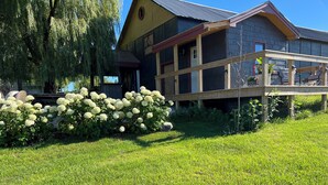 A house with a wooden deck, a covered porch, and a garden with white flowers. - Perfect 1-bedroom  off barn with AC in charming Petoskey (Petoskey)
