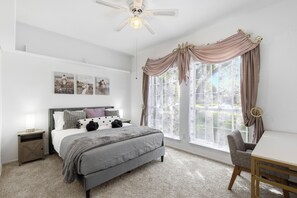 A bedroom with a bed, bedside table, chair, and a window with curtains. - Velvet Paradise-6 bdrm estate with pool, hot tub, tiki bar and firepit (Mesquite)