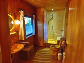 A wooden cabin bathroom with a sink, toilet, shower, and a window with curtains. - The perfect place to do nothing | A wooden house nestled between the forest and meadows (Geestland)