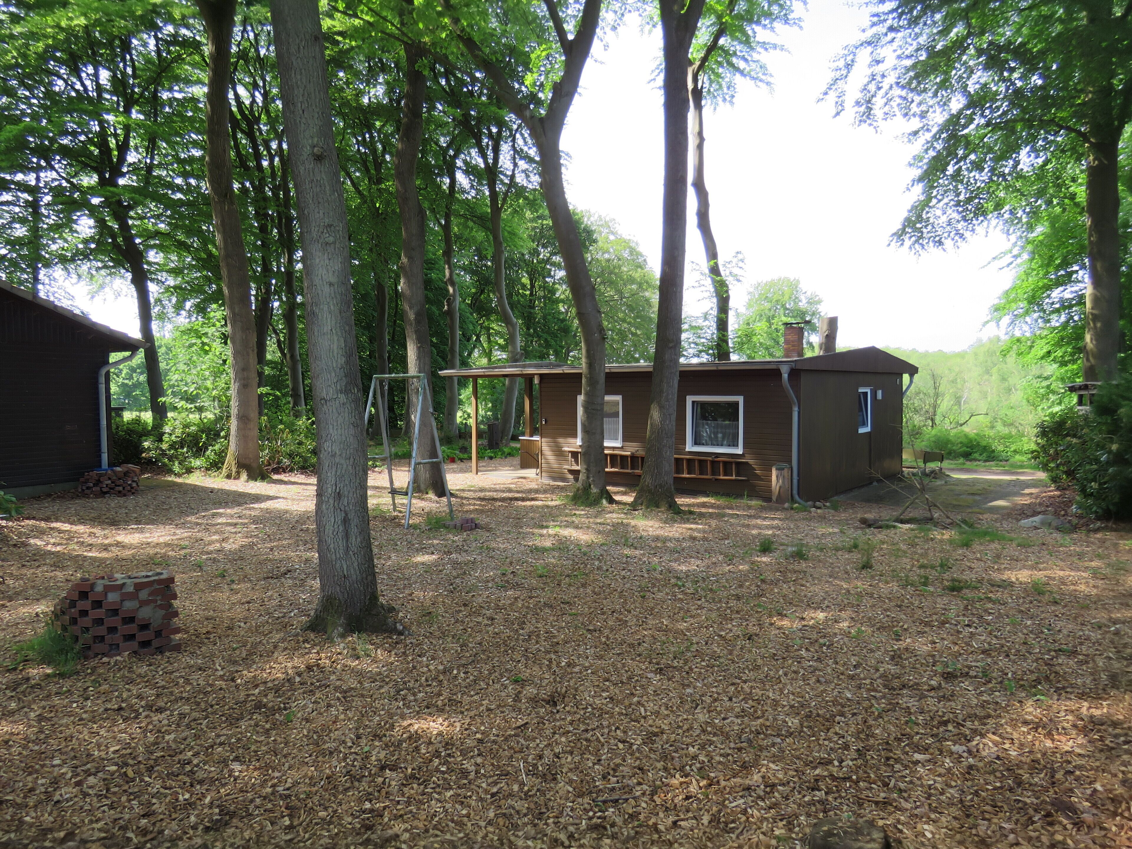Une cabane dotée d’un porche, entourée d’arbres et d’une pile de bois de chauffage.