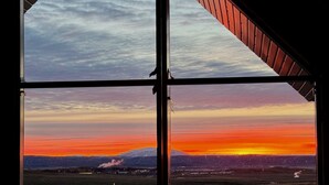 Een kamer met een groot raam, met uitzicht op een berglandschap in de zonsondergang.